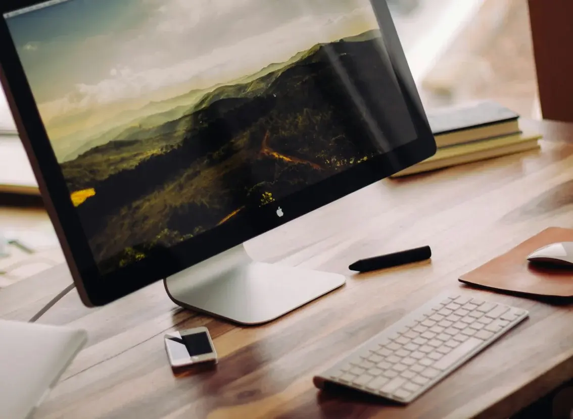 Ordenador de sobremesa con un paisaje de montaña en la pantalla, sobre una mesa de madera