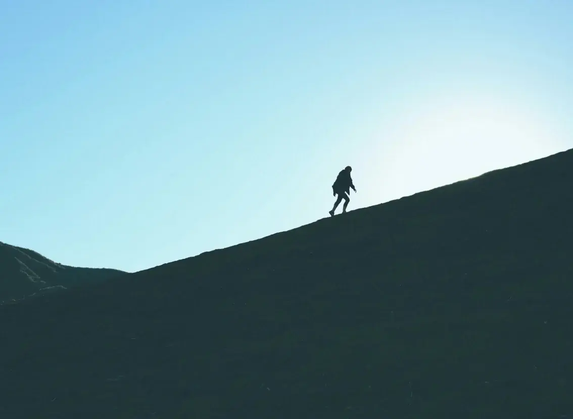 Silueta de una persona que sube una ladera a contraluz